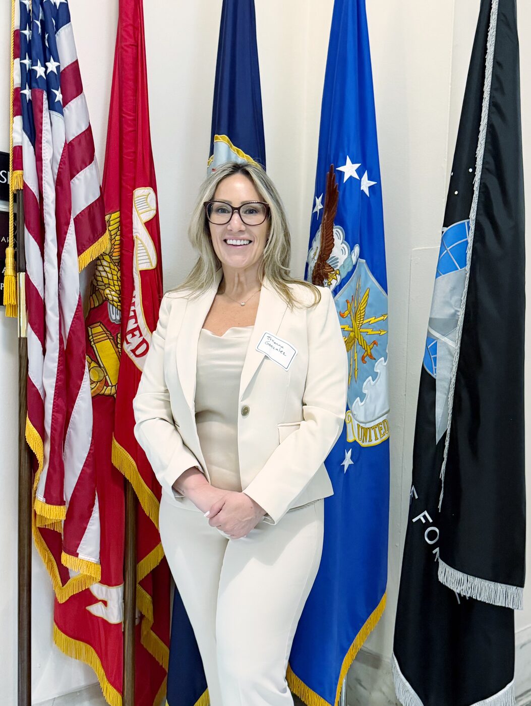 Jovianna Gonzalez at a U.S. government engagement, standing before the United States armed forces service flags